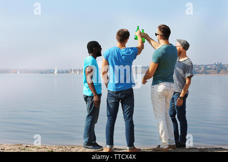 Les jeunes hommes de boire une bière au bord de la rivière Banque D'Images