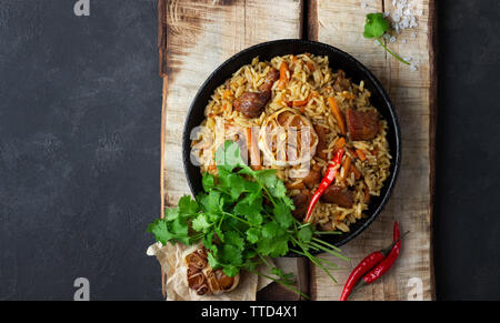 Cuisine orientale. Pilaf ouzbek ou plov du riz et de la viande dans une poêle en fonte sur bois. rustique Vue de dessus avec copie espace. Banque D'Images