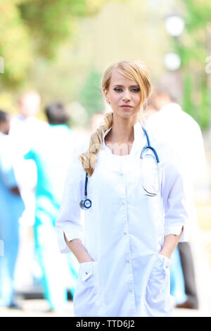 Smart belle femme médecin avec presse-papiers en mains debout contre groupe de medecins floue Banque D'Images