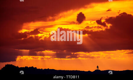 Silhouette Of Man Standing On Mountain Desert Ridge dans Arches National Park dans le cadre de spectaculaire coucher de soleil Nuages et rayons de soleil Banque D'Images