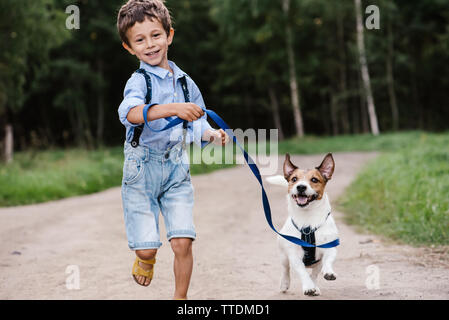 Heureux garçon au chien en laisse tourner au country road Banque D'Images