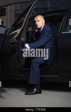 Young handsome businessman wearing costume bleu foncé assis dans sa voiture Banque D'Images