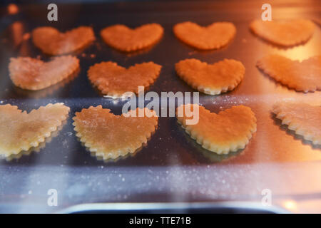 Des biscuits en forme de coeur non cuites sur une plaque de cuisson dans un four Banque D'Images