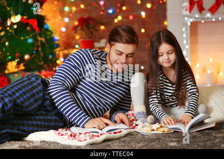 Grand frère avec sa petite sœur la lecture de livres et de manger des biscuits de Noël dans la salle de séjour Banque D'Images