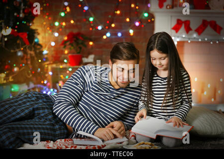 Grand frère avec sa petite sœur la lecture de livres et de manger des biscuits de Noël dans la salle de séjour Banque D'Images