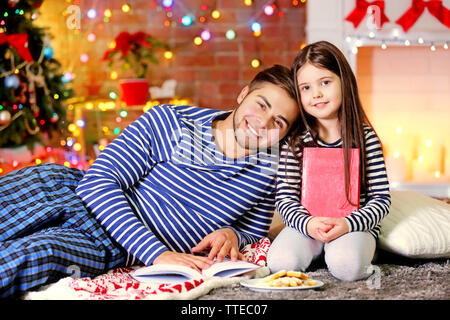 Grand frère avec sa petite sœur la lecture de livres et de manger des biscuits de Noël dans la salle de séjour Banque D'Images