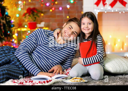 Grand frère avec sa petite sœur la lecture de livres et de manger des biscuits de Noël dans la salle de séjour Banque D'Images