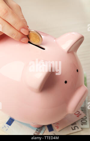 Woman's hand putting euro pièce dans une tirelire sur la table. Concept d'épargne financière Banque D'Images