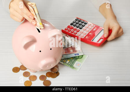 Woman's hands mettant en euros dans une tirelire et compter avec la calculatrice sur la table. Concept d'épargne financière Banque D'Images