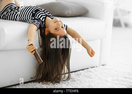 Cute little girl chante dans un micro imaginer allongé sur un canapé dans la chambre moderne Banque D'Images