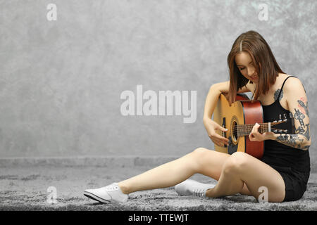 Attractive Woman with tattoo à jouer de la guitare sur fond gris Banque D'Images