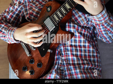 Jeune homme jouant de la guitare électrique sur canapé gris à la maison Banque D'Images