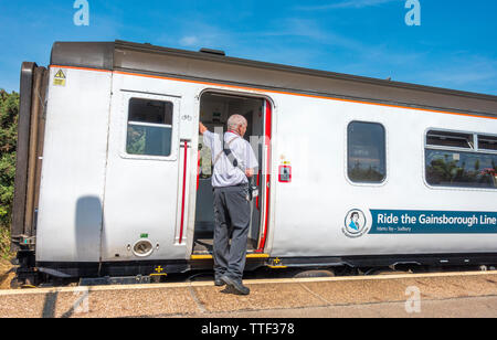 Les hommes d'âge moyen employé, debout sur la plate-forme, portant des ticket machine, appuyer sur le bouton pour le train de quitter West Runton, Norfolk, Angleterre, Royaume-Uni. Banque D'Images