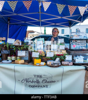 Une femme d'âge moyen debout derrière son étal, la vente du fromage à Norfolk un marché en plein air, dans la région de Sheringham, North Norfolk, Angleterre, Royaume-Uni. Banque D'Images