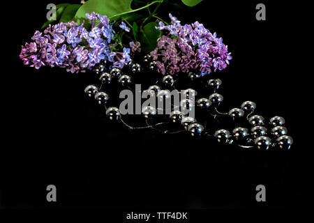 L'argent métallique en forme de boule perles et lilas avec des feuilles vertes sur fond noir. Banque D'Images