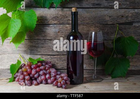Bouteille de vin de vigne et le verre de vin sur un fond de feuillage vert et de vieux panneaux en bois Banque D'Images