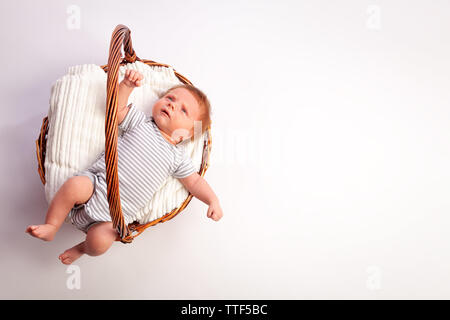 Portrait d'un bébé nouveau-né garçon, âgé de 1 mois, dans un body à rayures, cheveux roux, yeux bleus sur literie blanche dans un panier en osier sur un bac isolé blanc Banque D'Images