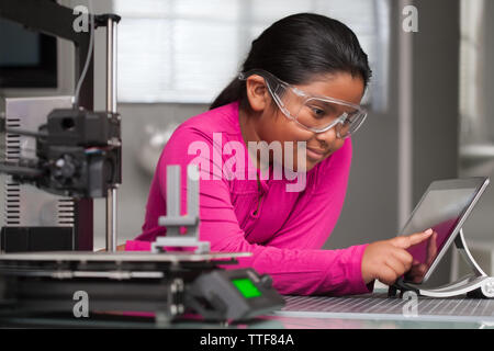 Un jeune étudiant portant le rose est de travailler sur un écran tactile apporte des modifications à un 3d printed jouet dans une école d'été tech class. Banque D'Images