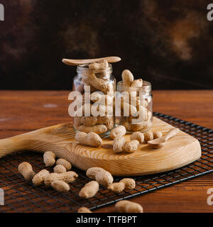Close-up d'arachides dans des bocaux avec du service et grille de refroidissement sur table en bois contre le mur Banque D'Images