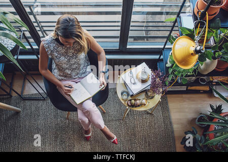 Vue de dessus de businesswoman writing in diary while sitting on chair at home office Banque D'Images