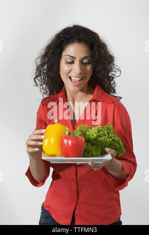 Femme tenant une assiette de légumes crus et souriant Banque D'Images