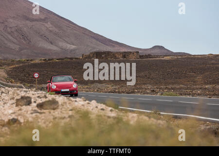 Voiture rouge conduite en route pavée vide dans un paysage volcanique du désert Banque D'Images