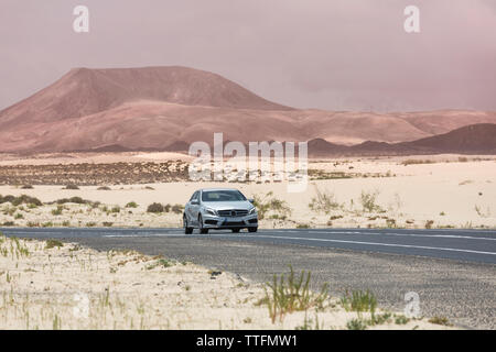 Voiture grise vide conduite route pavée dans les paysages volcaniques du désert Banque D'Images