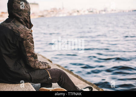 Young man wearing Hooded Jacket while sitting on steps au riverbank Banque D'Images