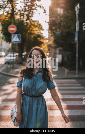 Jeune femme portant des lunettes de soleil pendant la traversée de route en ville Banque D'Images