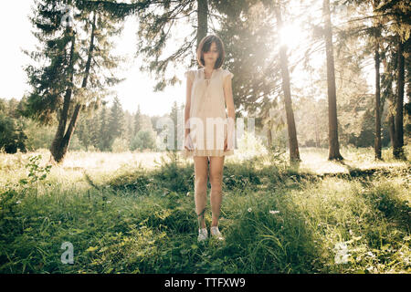 Toute la longueur de sad young woman standing on grassy field in forest Banque D'Images