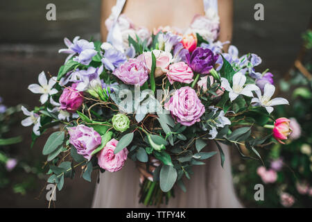 Bride holding b beau mariage coloré bouquet de roses, pivoines et tulipes dans un rose vif, corail et violet couleurs. Banque D'Images