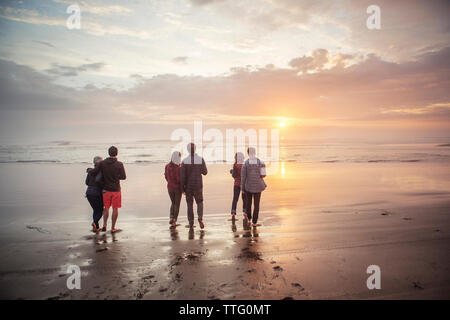 Vue arrière du couple à terre à la plage pendant le coucher du soleil Banque D'Images