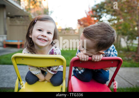 Close-up of smiling frères et sœurs à genoux sur des chaises dans la cour Banque D'Images