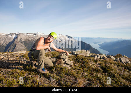 Climber s'accroupit à côté de cairn du sommet du pic escaladées auparavant. Banque D'Images