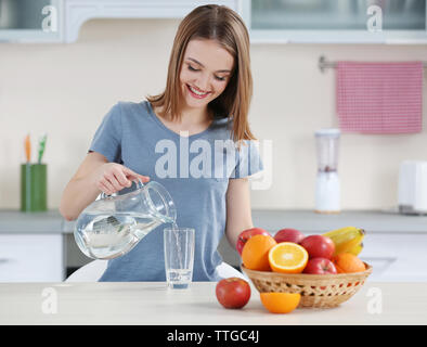 Jeune femme versant de l'eau à partir de la verseuse en verre dans la cuisine Banque D'Images