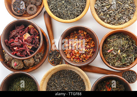 Variété de thé sec dans des pots et cuillères en bois isolé sur blanc Banque D'Images