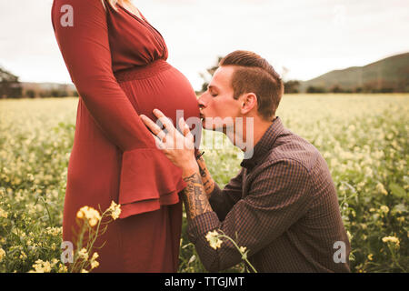 Man kissing pregnant wife's abdomen sur terrain against sky Banque D'Images