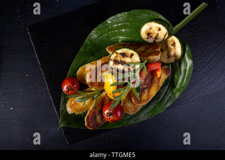 Vue de dessus de fromage halloumi grillé avec tomates cerises, poivrons et courgettes servi dans des feuilles sur la table Banque D'Images