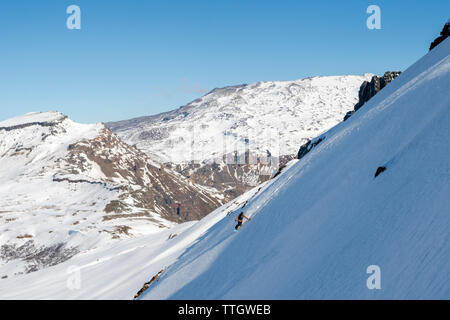 Une femme snowboards sur une journée ensoleillée. Un volcan peut être vu à l'arrière. Banque D'Images