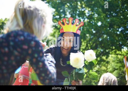 Happy woman wearing crown papier tout en donnant des roses blanches à l'adolescente pendant un anniversaire à cour Banque D'Images