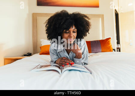 Businesswoman reading magazine on bed in hotel room Banque D'Images