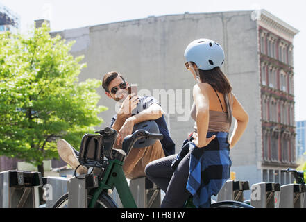 Happy man photographing woman sitting on bicycle in city Banque D'Images