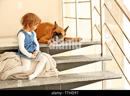 Petite fille mignonne avec boxer chien assis sur l'escalier piscine Banque D'Images