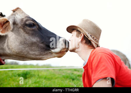 Side view of man kissing cow on grassy field against sky Banque D'Images