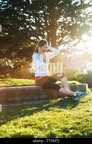 Jeune femme assise et talking on mobile phone au champ sur sunny day Banque D'Images