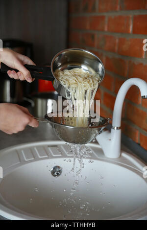 Les mains verser de l'eau de puits plus spaghetti bouillis dans la cuisine Banque D'Images