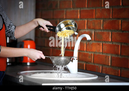 Les mains verser de l'eau bouilli de pâtes sur le lavabo dans la cuisine Banque D'Images