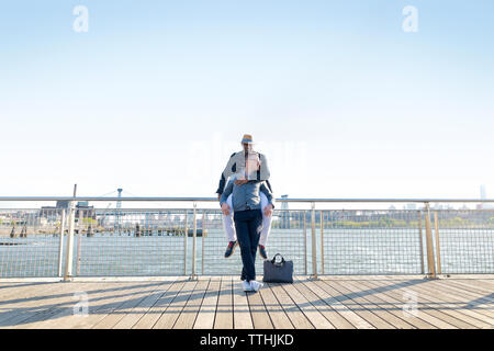 Happy man embracing boyfriend on pier by river contre ciel clair Banque D'Images