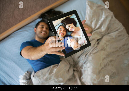 Vue supérieure de l'heureux couple prenant en selfies tablet while lying on bed Banque D'Images
