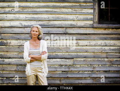 Portrait of woman with arms crossed standing contre cottage Banque D'Images